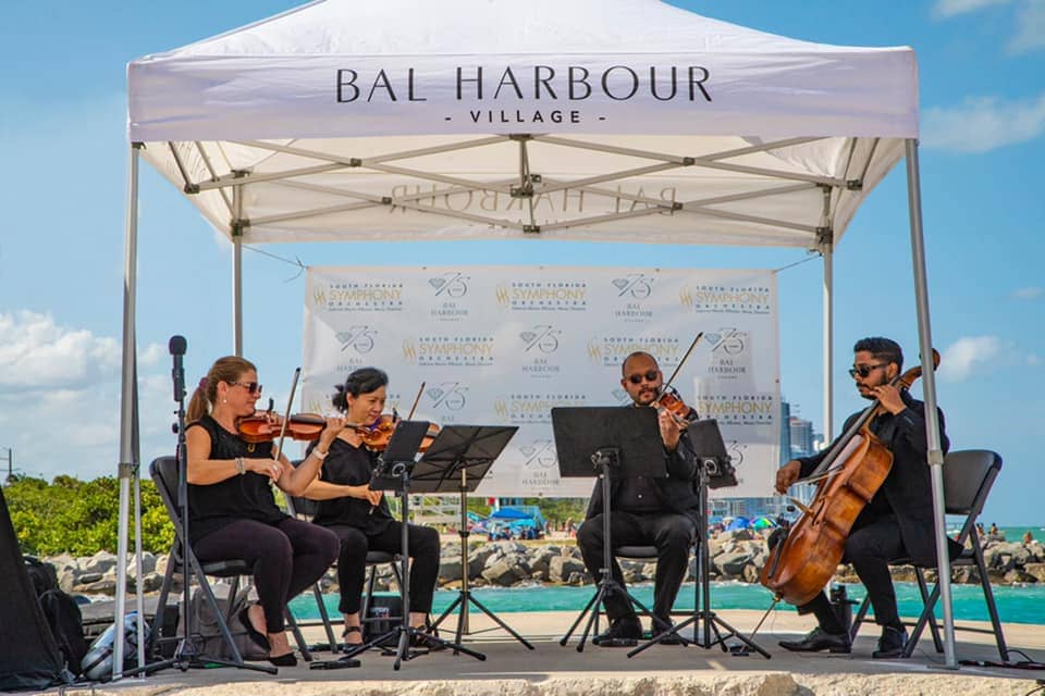 Four people playing instruments by the water