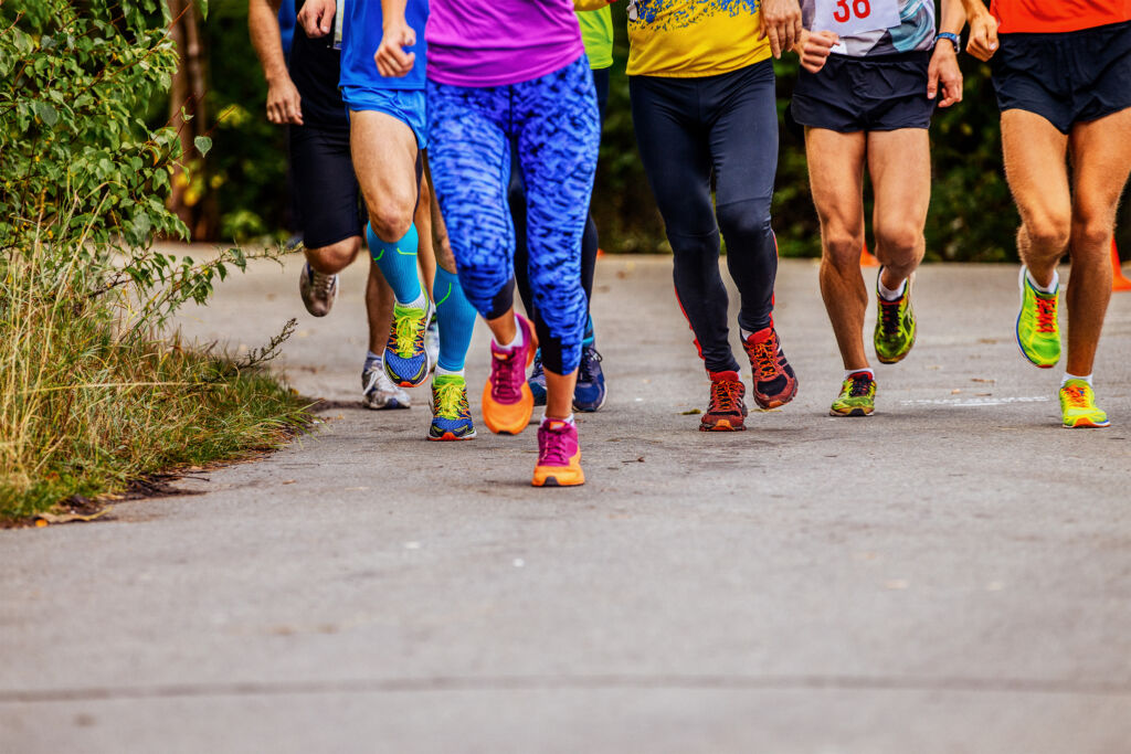 Legs of unrecognizable runners running on pavement in a 5K race.